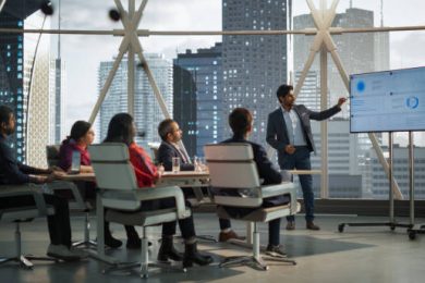 Booming Tech & Startup Ecosystem Diverse Indian Office Conference Room: Young South Asian CEO Makes a Presentation for Entrepreneurs, Talking, Using TV with Infographics and Statistics. Businesspeople Talk About an Ecommerce Startup