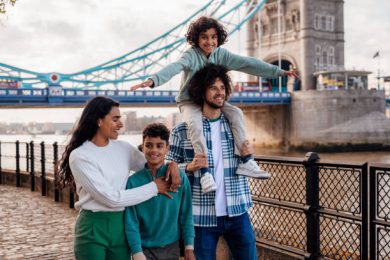 gettyimages-1680161294-612×612 A family happily walk along a riverside together with one of the sons on the father's shoulders.